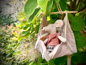 Kleine Stoffmaus in einer aufgehängten Stoffschaukel zwischen grünen Blättern