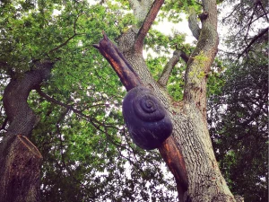 ein großer Baum, an dessen Stamm eine geschnitzte, riesige, hölzerne Schnecke emporkriecht
