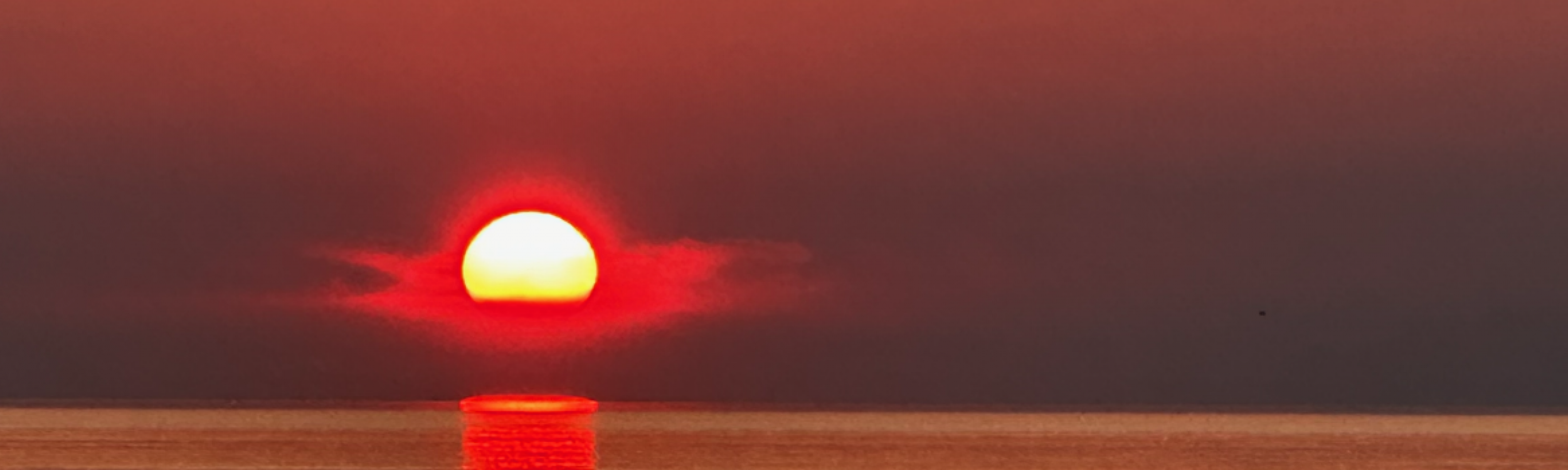 untergehende sonne über dem Meer, wirkt so, als taucht sie rot in das Wasser ein und geht am Horizont unter.